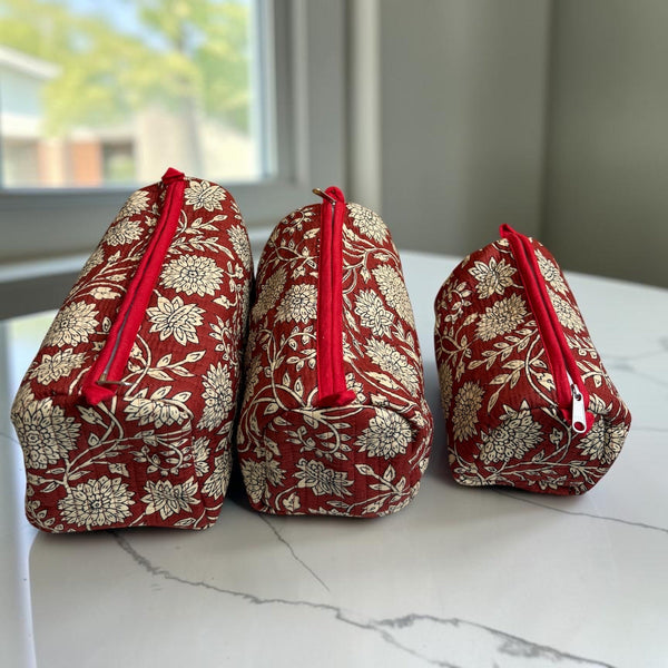 Three small zippered cosmetic pouches with a red and beige floral pattern, arranged on a white marble countertop in front of a window.