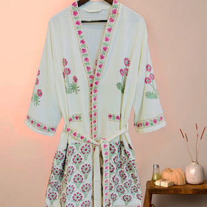 Light blue kimono-style robe with floral embroidery on a wooden hanger against a pink wall.