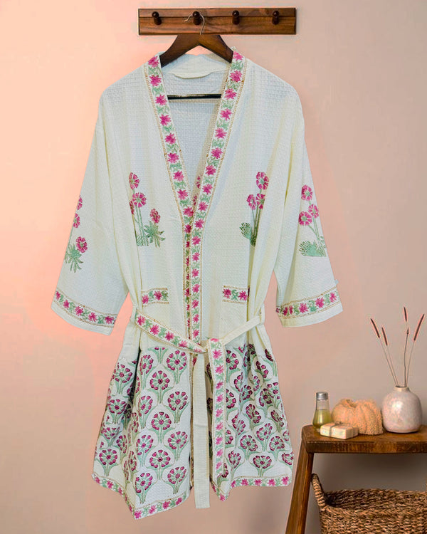 Light blue kimono-style robe with floral embroidery on a wooden hanger against a pink wall.