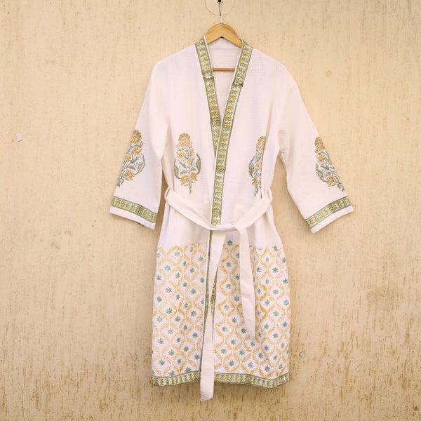 White robe with green and gold embroidery on a wooden hanger against a beige wall.