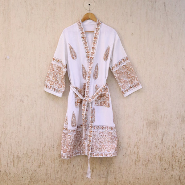 White robe with brown embroidery on a wooden hanger against a beige background