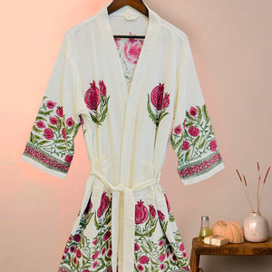 White robe with floral embroidery on a hanger against a pink wall.