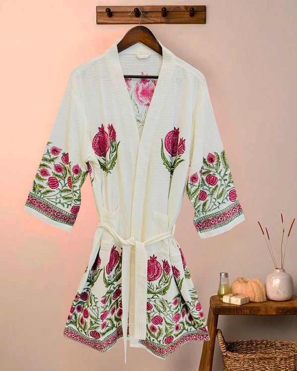 White robe with floral embroidery on a hanger against a pink wall.