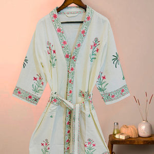 Floral embroidered robe on a hanger against a pink wall.