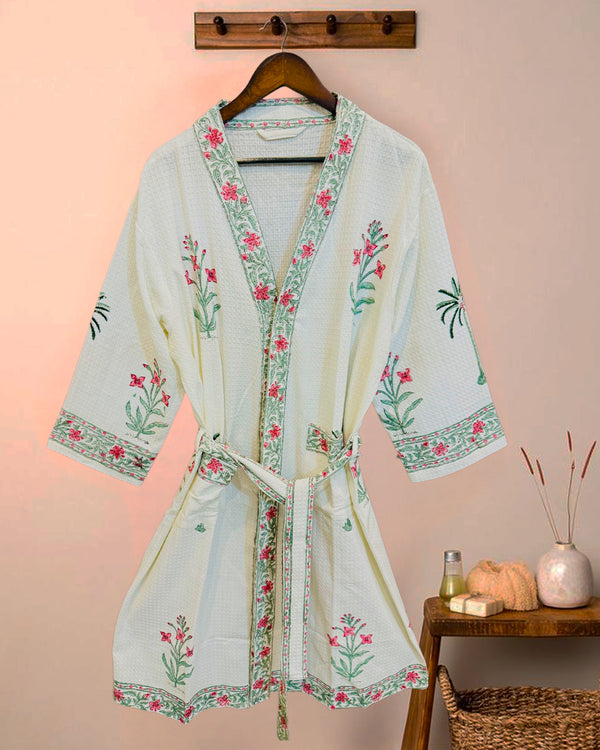 Floral embroidered robe on a hanger against a pink wall.