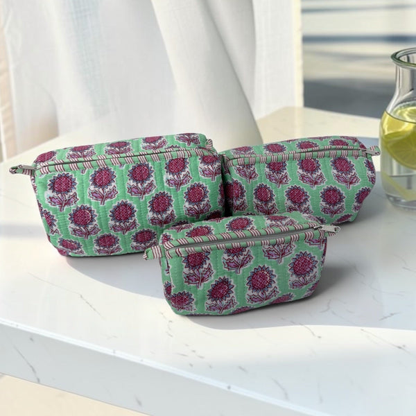 Three small zip pouches with a green and magenta floral pattern, arranged on a white marble table in front of white curtains.