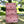 Three stacked zippered pouches in pink and white vertical stripes with small red hearts, displayed outdoors on a wooden table with a blurred garden background. A small white label on the bottom pouch reads 'newkasa'.