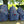 Three blue and white striped fabric pouches with red heart patterns and black-and-white braided zipper pulls, arranged on a light wooden table outdoors with trees in the background.