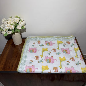 Children's blanket with animal pattern on a wooden surface next to a vase with flowers.